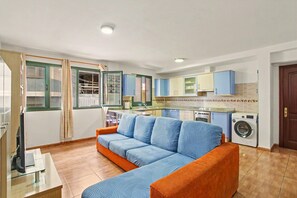 A living room with a sofa, a washing machine, and a kitchen area.