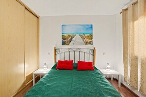 Ein Schlafzimmer mit einem Bett, zwei Nachttischen, einem Strandbild und einem Holzschrank.