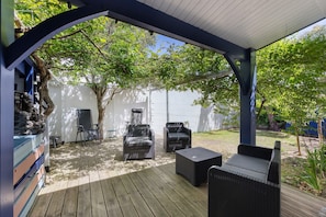 Un patio techado al aire libre con mobiliario de mimbre, una terraza de madera y una pared blanca al fondo.