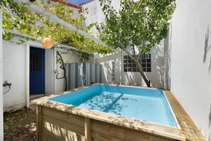 Una piscina rectangular con estructura de madera, rodeada por un muro blanco y una puerta azul.