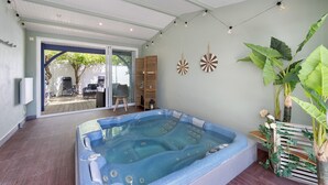 Un espace bien-être comprenant un jacuzzi, des étagères en bois et une grande plante.