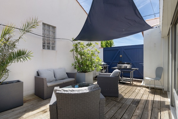 Un patio con mobiliario exterior, una parrilla y un gran paraguas que da sombra.