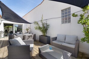Un patio con mobiliario de mimbre, una planta en maceta y una mesa de vidrio.