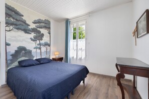 Un dormitorio con cama, mesita de noche, escritorio, ventana y pared decorada con un mural de un árbol.
