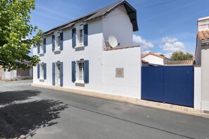 A two-story building with a white facade, blue shutters, and a satellite dish. - La Villa du Bonheur – Holiday Home with Jacuzzi (L'Aiguillon-la-Presqu'ile)