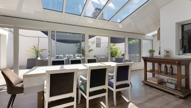 Un espace repas moderne doté d’un plafond en verre, de meubles blancs et d’un buffet en bois.