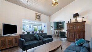 Un salon comprenant un téléviseur, des canapés, un meuble en bois et un coin repas visible à travers une porte vitrée.