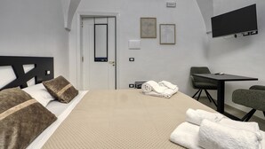 A hotel room with a bed, a desk, a chair, a TV, and an air conditioning unit.
