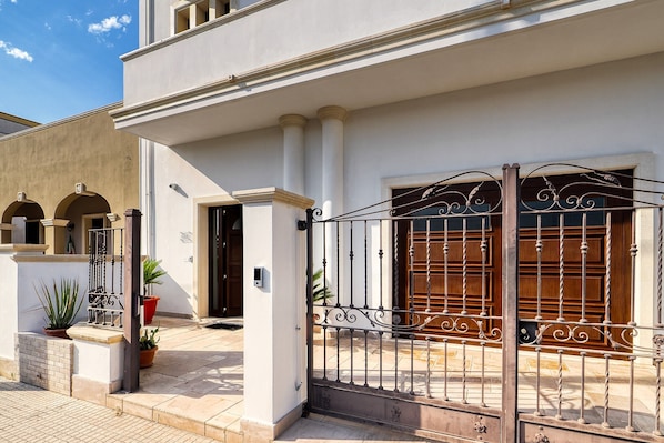 A building with a gated entrance, columns, and potted plants.