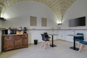 Eine moderne Küche mit Mikrowelle, Kaffeemaschine und einem Holzkasten. Zwei Stühle und ein kleiner Tisch mit einer Vase sind ebenfalls vorhanden.