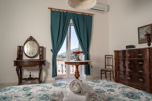 Una stanza arredata con un letto, una cassettiera, uno specchio, un tavolo con un vaso e una finestra con tende.