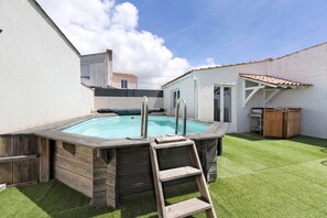 A hot tub with a wooden ladder, surrounded by a grassy yard and a white wall.