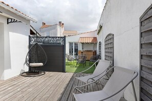 A wooden deck with two lounge chairs, a black gate, and a small garden area with chairs.