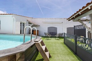 Piscina com deck de madeira, área coberta com cadeiras e jardim cercado.