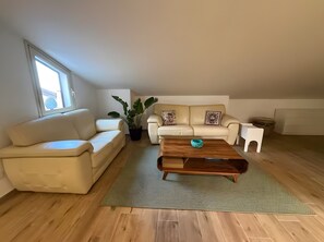 Ett modernt vardagsrum med en soffa, ett soffbord, en krukväxt och ett fönster.