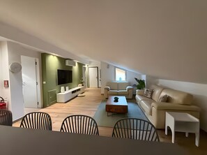 Ett modernt vardagsrum med en platt-TV, en soffa, ett soffbord och en matplats med stolar.