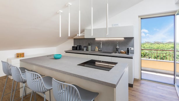 Una cocina moderna con una isla central, taburetes de bar, un amplio ventanal con vistas e iluminación colgante.