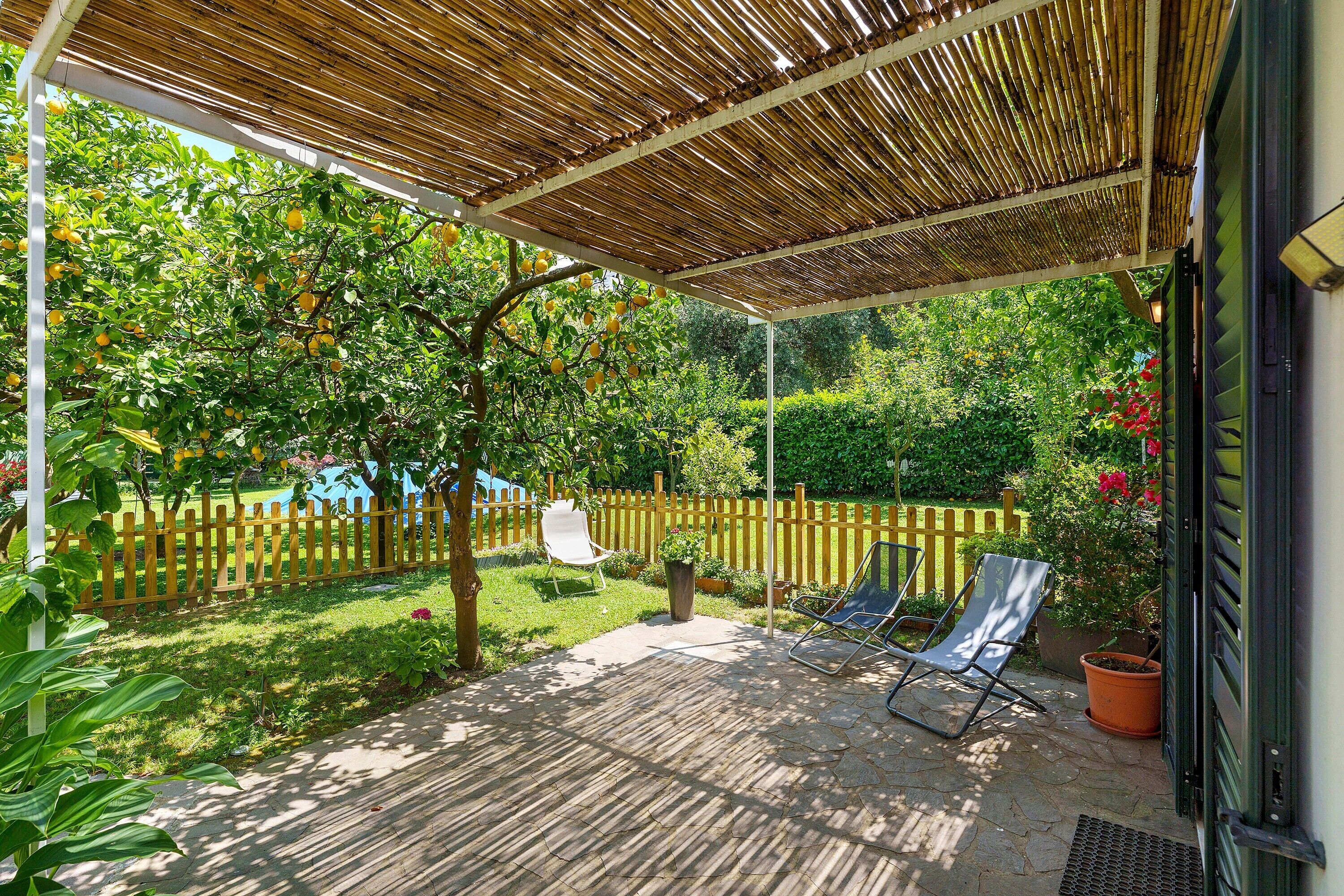 Una veranda riparata con pavimento in legno, due poltrone, una pianta in vaso e un recinto in legno.
