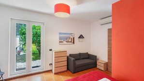 Ein Schlafzimmer mit einer Schiebetür zu einem Balkon, einem grauen Sofa, einer hölzernen Kommode, einem roten Teppich und einer roten Wand.