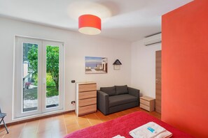 Ein Schlafzimmer mit einer Schiebetür zu einem Balkon, einem grauen Sofa, einer hölzernen Kommode, einem roten Teppich und einer roten Wand.