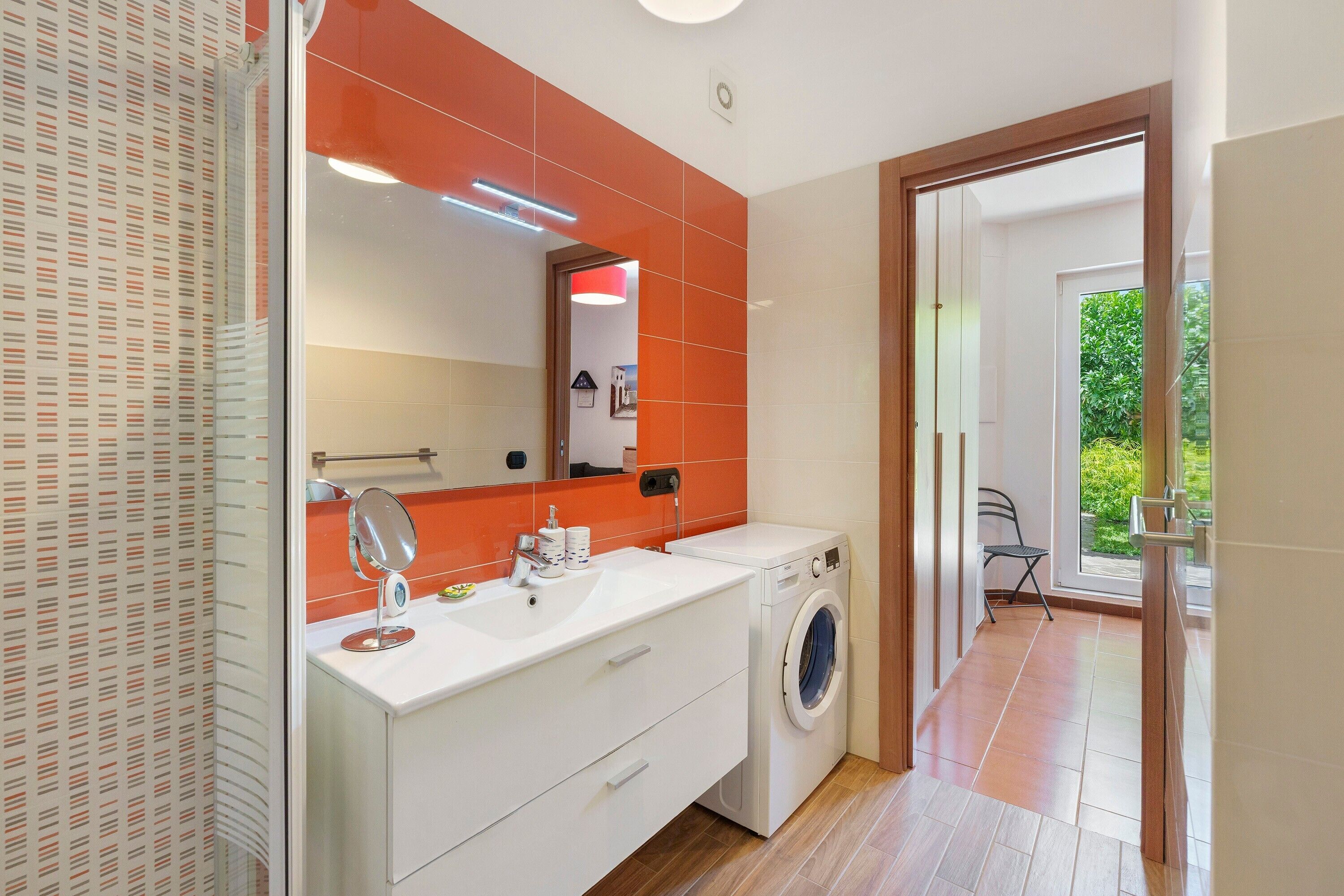 Un baño moderno con un espejo grande, lavamanos blanco y una lavadora.