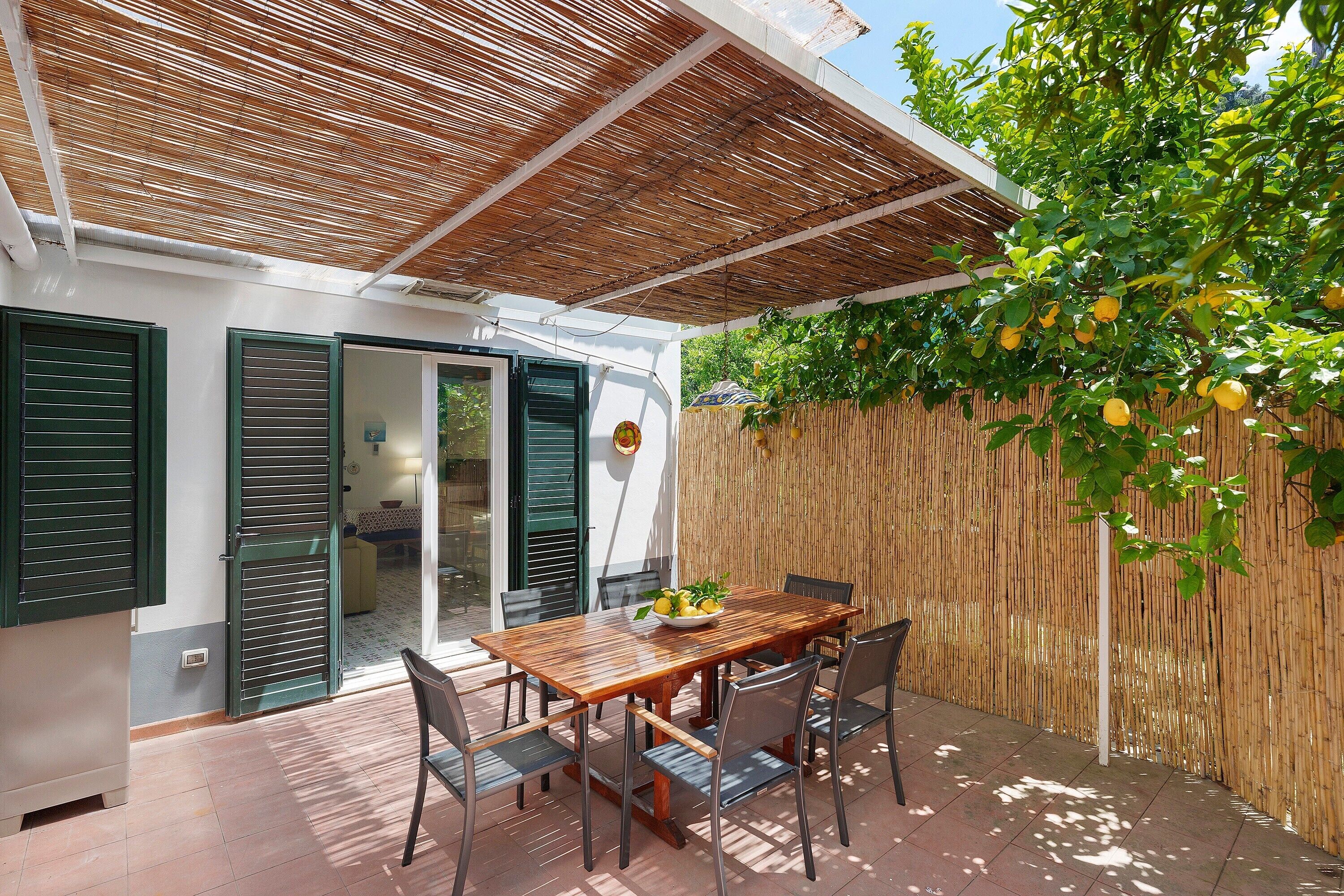 Un patio con tavolo e sedie in legno, una recinzione in bambù e un albero da frutto.
