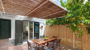 Eine Terrasse mit einem Holztisch und Stühlen, einem Bambuszaun und einem Baum mit Früchten.