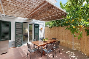 Eine Terrasse mit einem Holztisch und Stühlen, einem Bambuszaun und einem Baum mit Früchten.
