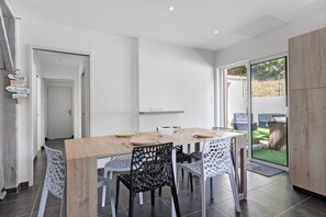 A dining area with a wooden table, chairs, and a view of the backyard through a glass door. - Holiday Home 'Ca M'Suffit' with Private Heated Pool, Terrace and Garden (La Tranche-sur-Mer)