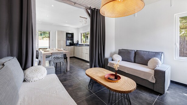 A modern living room with a sofa, a dining table, and a kitchen in the background.