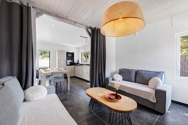 A modern living room with a sofa, a dining table, and a kitchen in the background.
