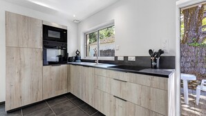 A modern kitchen with a built-in oven, microwave, and sink, with a view of a tree outside.