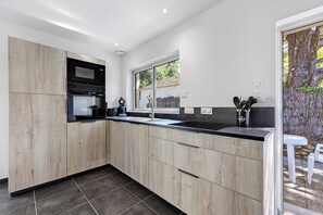 A modern kitchen with a built-in oven, microwave, and sink, with a view of a tree outside.