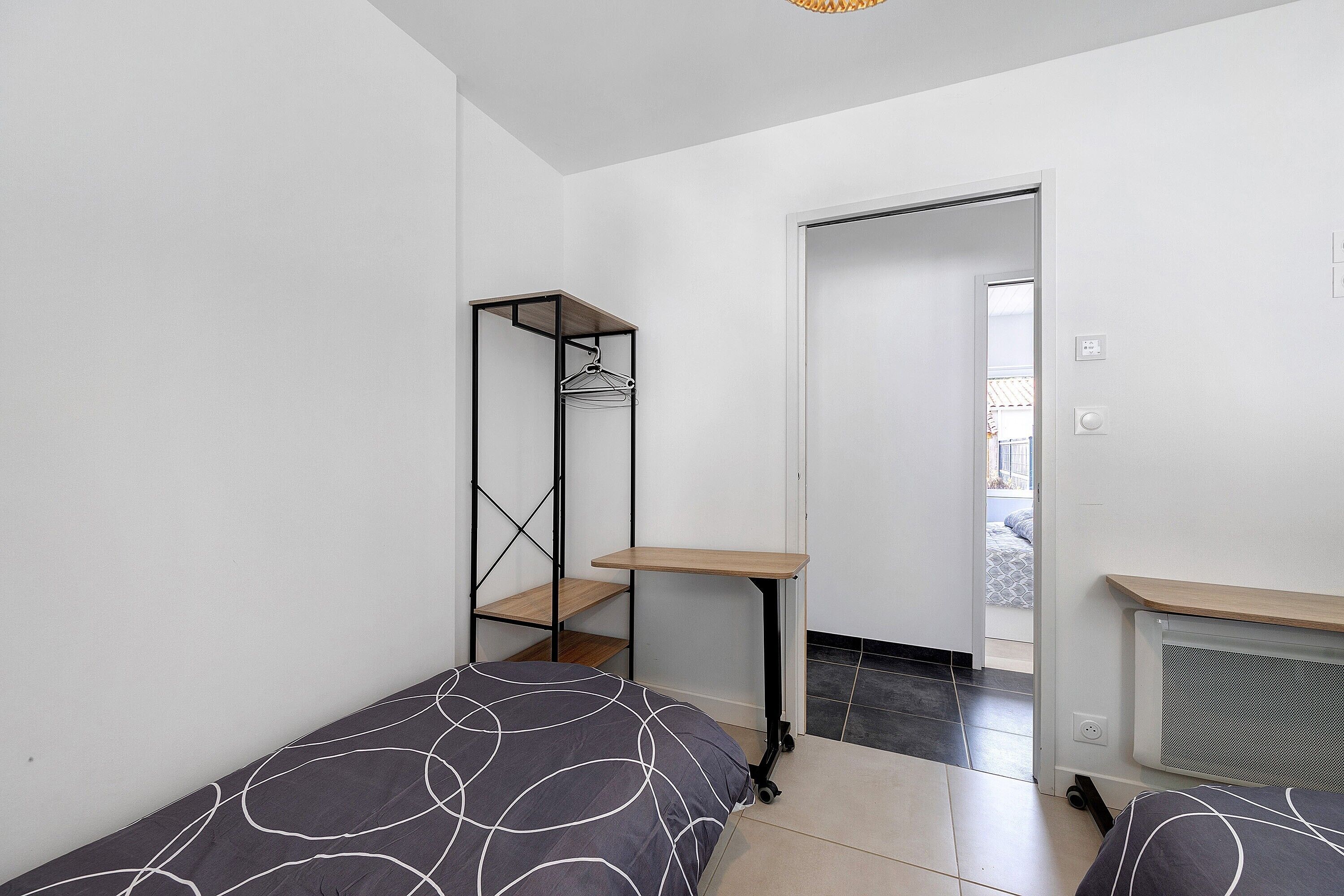 Une chambre à coucher avec un lit, une petite table, une étagère et un radiateur.