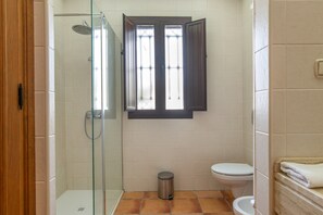 Une salle de bain avec une douche à parois de verre, des toilettes et une fenêtre dont les volets sont ouverts.