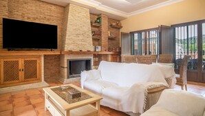 Ein Wohnzimmer mit Kamin, Fernseher, einer Couch und einem Essbereich mit Stühlen.