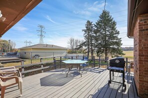 A wooden deck with a grill, chairs, and a pool.