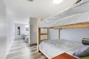 A bunk bed room with a wooden frame, a white mattress, and a green pillow. There is a wooden door and a small window.