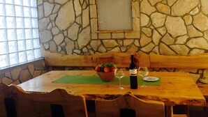 Un mur de pierres, une table en bois, des chaises, un panier de fruits, des verres à vin et une bouteille.