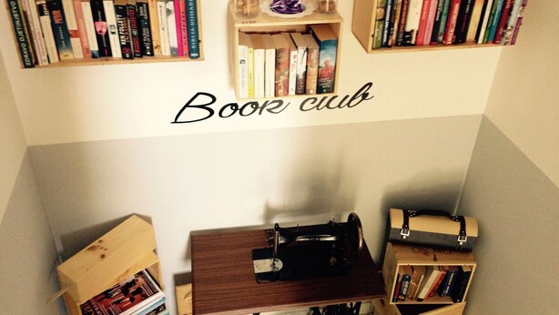 Une pièce comprenant une machine à coudre, des étagères en bois et un panneau indiquant « Club de lecture ».