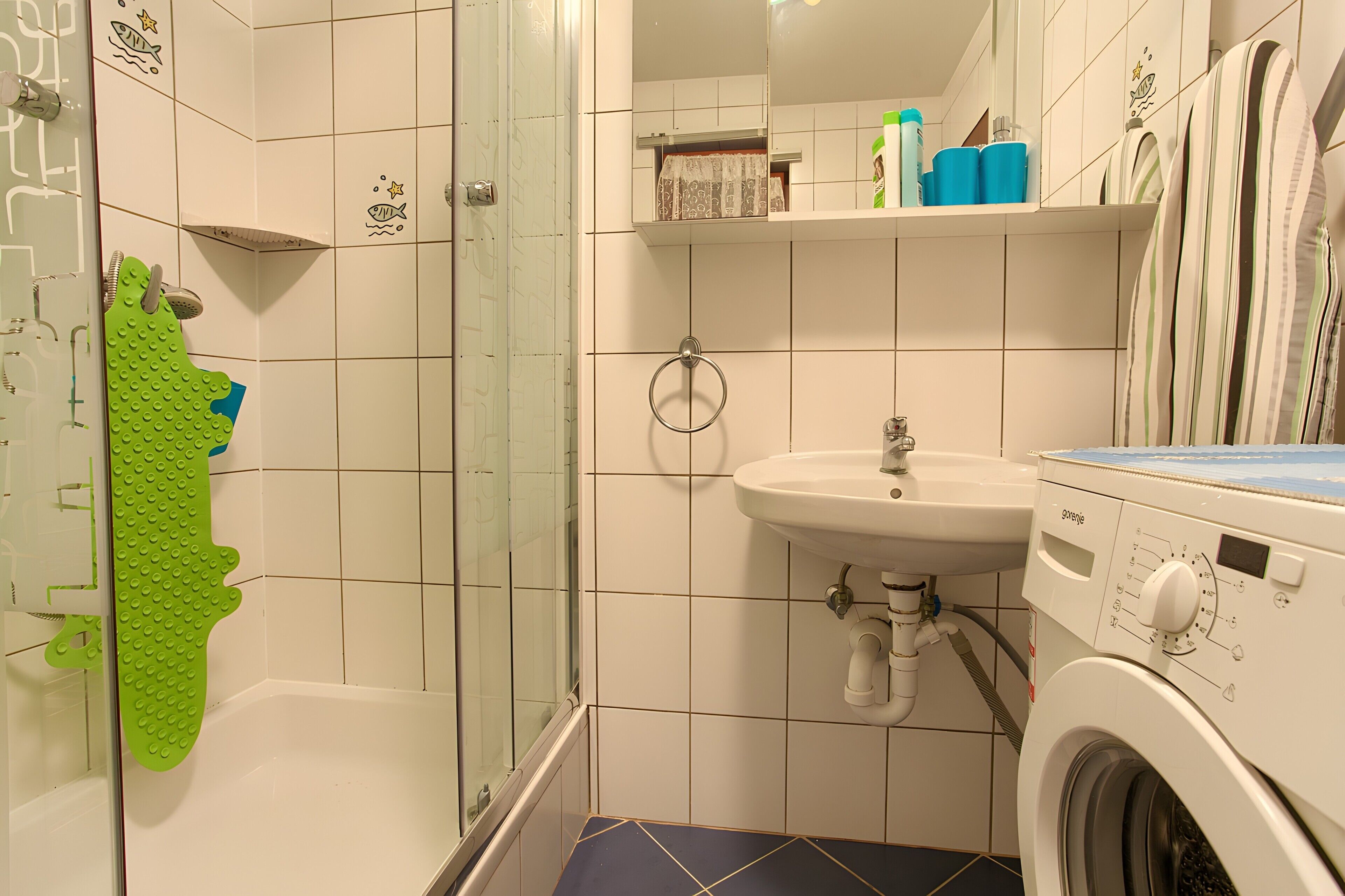 Ein Badezimmer mit Duschkabine, Waschbecken, Waschmaschine und Handtuchhalter.