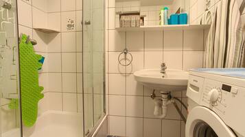 Ein Badezimmer mit Duschkabine, Waschbecken, Waschmaschine und Handtuchhalter.
