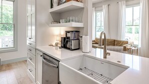 A modern kitchen with a dishwasher, coffee maker, and a sink with a wire rack. - Carlton Landing-Cottage on Hill (Carlton Landing)