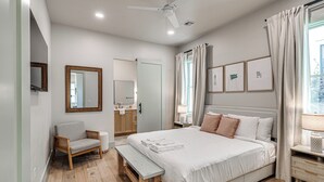 A modern bedroom with a bed, bedside table, chair, and a large window with curtains. - Carlton Landing-Cottage on Hill (Carlton Landing)
