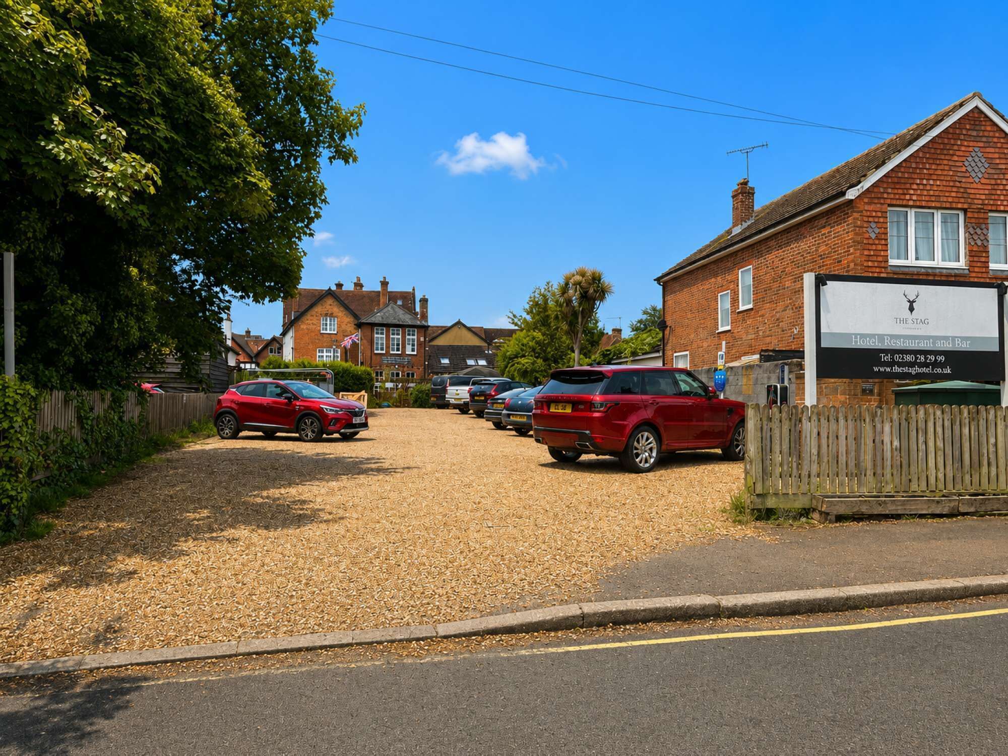 A red car parked in a gravel driveway with a brick building labeled 'The Stag Hotel, Restaurant and Bar' in the background.
