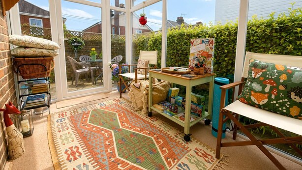 A conservatory with a patterned rug, a table with books, and a chair with a fox-patterned cushion. - Charming 2BR Cottage in the Heart of Lyndhurst | Parking & Garden (Lyndhurst)
