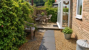 A patio with a table and chairs, surrounded by greenery and a brick wall. - Charming 2BR Cottage in the Heart of Lyndhurst | Parking & Garden (Lyndhurst)