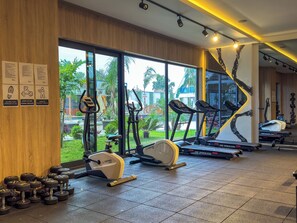 Ein Fitnessraum mit Trainingsgeräten, großen Fenstern und Blick auf Grünfläche.