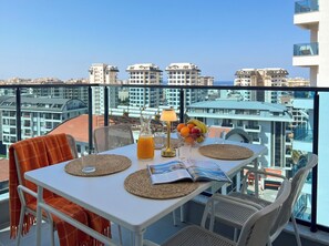 Ein Balkon mit Tisch für zwei Personen, ausgestattet mit einer Zeitschrift, einer Obstschale und einem Glas Orangensaft.