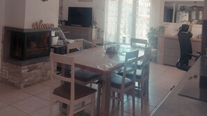 Un salon avec une cheminée, une table à manger avec des chaises, un téléviseur et un coin cuisine équipé d’un réfrigérateur.